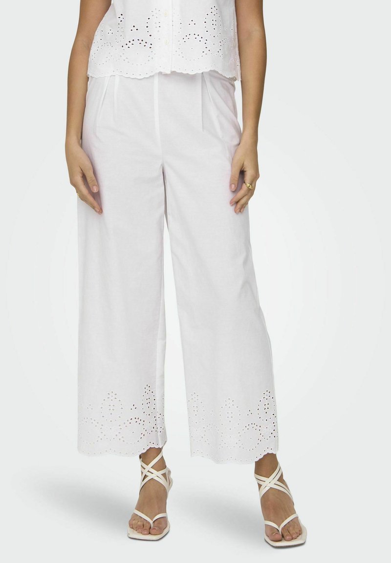 Witte, wijde broeken met geborduurde eyelet-details aan de zoom, gecombineerd met witte strap sandalen. Zachte stof en een relaxte pasvorm.