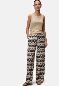 Débardeur en maille beige associé à un pantalon large à motif zigzag multicolore. Texture lisse avec une coupe décontractée. Sandales marron.