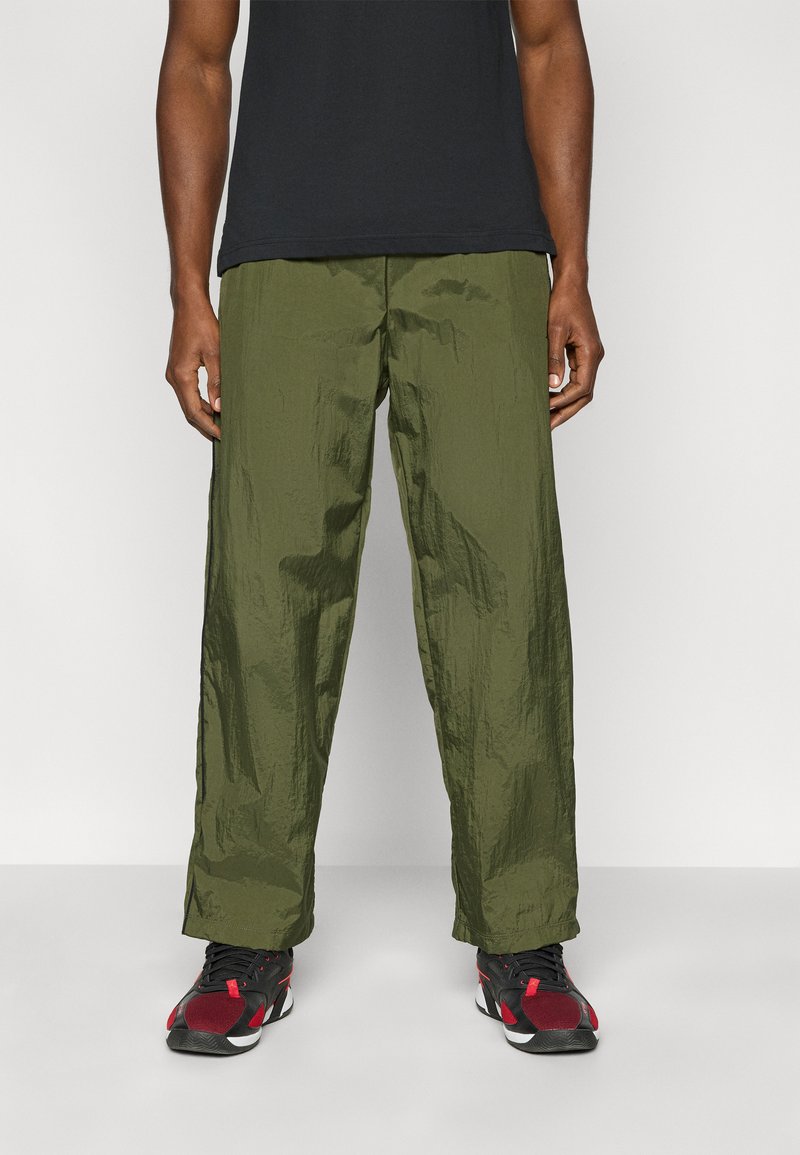 Παντελόνι από ελαφρύ ύφασμα σε ελιά πράσινο χρώμα, με ρυτιδιαστή υφή και φαρδιά εφαρμογή. Φορεμένο με μαύρα και κόκκινα αθλητικά παπούτσια. Απλό μαύρο μπλουζάκι από πάνω.