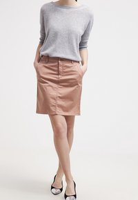Maglione grigio chiaro con maniche a tre quarti, abbinato a una gonna a tubino color pesca con passanti per cintura e tasche laterali. Tacchi neri e argento.