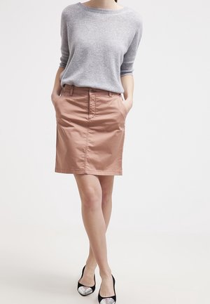 Un pull gris clair à manches trois-quarts, assorti à une jupe crayon couleur pêche avec passants de ceinture et poches latérales. Des escarpins noirs et argentés.