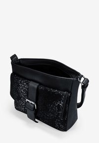 Bolso cruzado negro con solapa frontal texturizada, hebilla plateada, correa ajustable y parte superior abierta que muestra un bolso con cremallera en el interior.