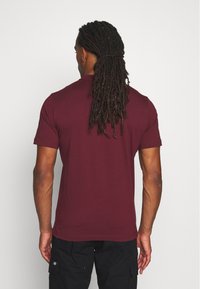 Bordó polo triko s krátkými rukávy, hladká textura, přiléhavý střih a žádné viditelné vzory, nošeno s černými cargo kalhotami.