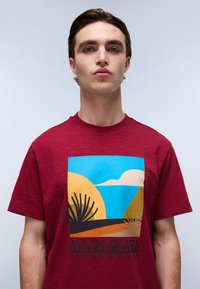 Bordo majica s kratkimi rokavi z grafičnim tiskom, ki prikazuje puščavske pokrajine, moder nebo, sonce in črne sličice kaktusov. Tkanina iz bombažne mešanice.