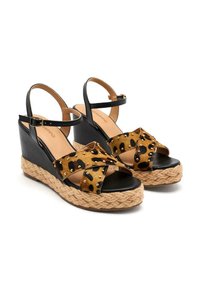 Sandales en coin avec des sangles en cuir noir et une tige en imprimé léopard ornée de clous dorés. Semelle en jute de style espadrille avec une texture tressée.