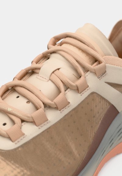 Scarpa da ginnastica rosa chiaro con tomaia in rete, fissata da lacci piatti intrecciati. Presenta un motivo testurizzato e una suola in gomma chiara con accenti.