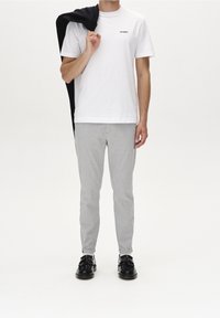 Vit bomull T-shirt med svart logotyp, gråmönstrade skräddarsydda byxor och svarta skor med tofsar. Svart tröja hängande över axeln.