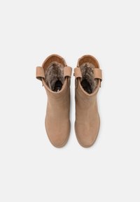 Bottines beiges en cuir suédé lisse, doublées de fourrure, avec des tirettes sur les côtés. Embouts ronds et semelles plates pour plus de stabilité.