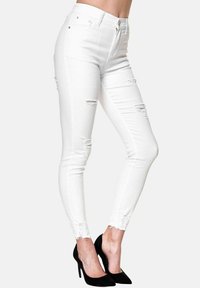 Jeans blancos, ajustados y con desgastes en los muslos y dobladillos deshilachados. Combinados con zapatos de tacón negros.