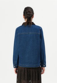 Jeans jakna u tamnoplavoj boji s smešanim kožnim ovratnikom, dugim rukavima i dugmadima na manžetama, koja ima klasičan kroj i detalj na leđima.