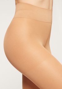 Beige transparente Strumpfhosen mit glatter Textur und breitem, elastischem Bund, der eng am Bein anliegt. Keine sichtbaren Muster oder Beschläge.