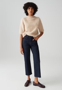 Light beige fluffy sweater with a round neckline, paired with dark blue cropped jeans and burgundy loafers, set against a plain background.
