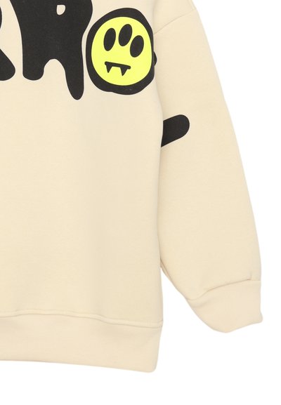 Felpa beige con un grande design grafico nero che presenta un volto sorridente giallo con zanne. Include polsini e orlo a coste.