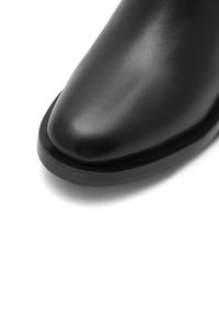 Melna ādas potīšu zābaks ar gludu tekstūru, smailu degunu un izturīgu gumijas zoli. Minimalistisks dizains bez redzamiem stiprinājumiem.