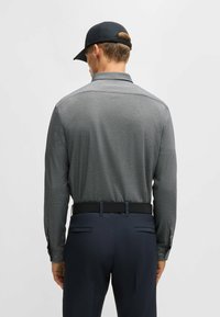 Långärmad, kolgrå skjorta med knappar och strukturerad yta, med klassisk krage och kontrasterande mörk midja. Kepa syns inte.