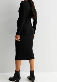 Robe midi noire côtelée avec manches longues, silhouette ajustée et encolure ronde, associée à des bottines noires à talon carré.