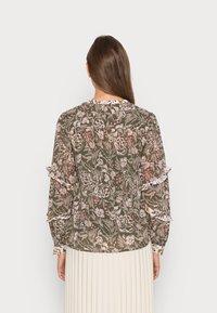 Blusa floral em verde-oliva, com padrões florais em rosa e branco, mangas com babados e decote redondo com acabamento decorativo.
