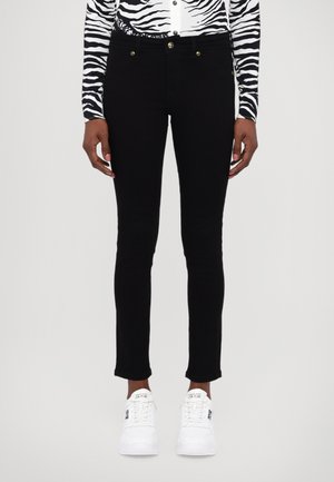 Pantalons slim noirs avec des accents de boutons dorés et un ourlet brut, associés à des baskets blanches. Haut à motif zèbre visible à la taille.