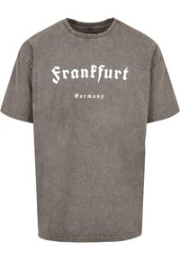 Šedé oversized tričko s opraným vzhledem, na kterém je v kontrastním bílém gotickém písmu vytištěno 'Frankfurt' a 'Německo'. Krátké rukávy.