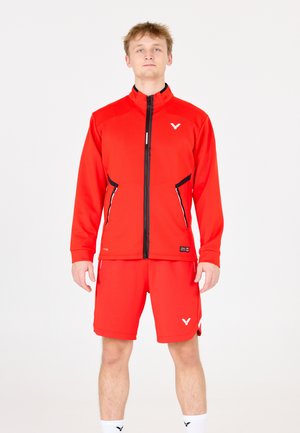 Rød atletisk jakke med sorte detaljer og lynlåslommer, sat sammen med matchende røde shorts. Fremstillet af glat, strækbart stof.