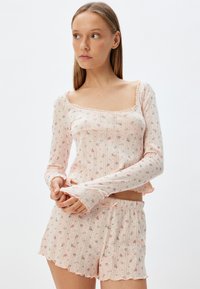Ensemble de pyjama rose clair avec un haut à manches longues et un short. Présente des motifs floraux, des bords festonnés et une texture côtelée. Design de vêtement de loisirs.