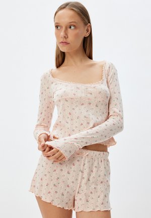 Ensemble de pyjama rose clair avec un haut à manches longues et un short. Présente des motifs floraux, des bords festonnés et une texture côtelée. Design de vêtement de loisirs.