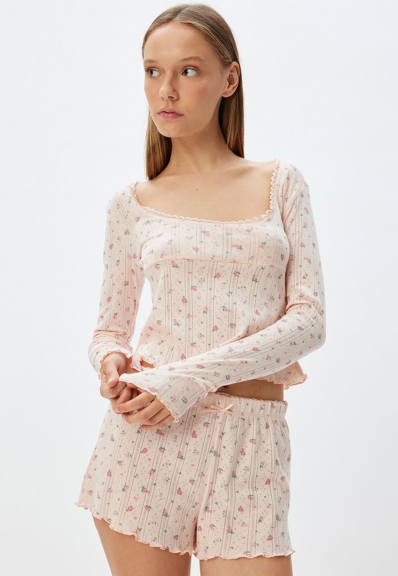 Ensemble de pyjama rose clair avec un haut à manches longues et un short. Présente des motifs floraux, des bords festonnés et une texture côtelée. Design de vêtement de loisirs.