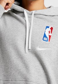 Sweat à capuche gris en tissu doux, avec un logo Nike blanc et un logo NBA brodé en rouge, bleu et blanc sur la poitrine.