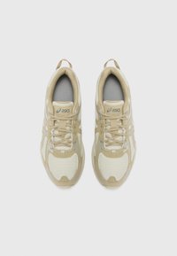 Beige athletic shoes with mesh and synthetic uppers, featuring reflective silver accents, round toe, lace-up design, and padded collars.