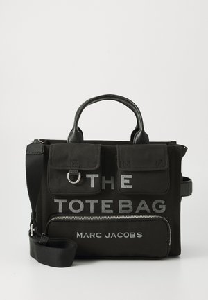 Sort canvas tote taske, der har "THE TOTE BAG" og "MARC JACOBS" i fed hvid skrift, med en lynlåslomme og to topgreb.
