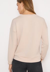 Sweatshirt beige clair avec un col rond et des emmanchures tombantes. Il présente des poignets et un ourlet côtelés, fabriqué à partir d'un matériau doux avec une texture minimale.