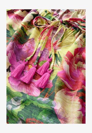 Haut en tissu floral jaune, rose et vert avec un col froncé. Doté de trois pompons roses attachés à des cordons.
