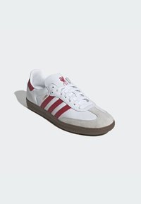 Baskets Adidas Samba basses blanches et rouges avec lacets blancs, semelle en gomme, et logo de Liverpool FC sur la languette, le texte sur le côté indique "SAMBA".