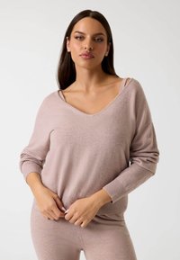Suéter rosa claro con escote en V, de manga larga y dobladillo acanalado. Textura suave y corte relajado, evidente a través de pliegues suaves.