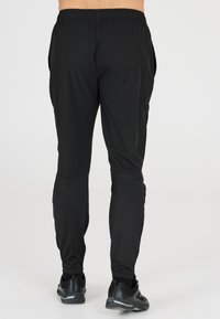 Zwarte sportbroek met een tapered fit, elastische tailleband en zijzakken. Gemaakt van een lichtgewicht, gladde stof met een lichte glans.