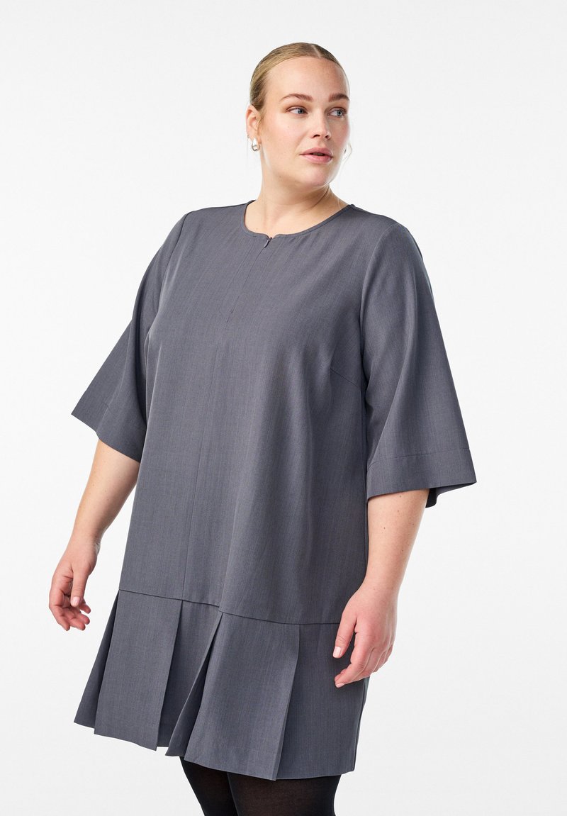 Šedé šaty s krátkými rukávy, kulatým výstřihem a sklady na spodním lemu. Jsou vyrobeny z hladké tkaniny s jemnou texturou.
