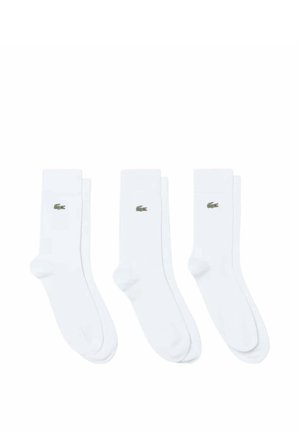 Tre paia di calzini bianchi crew disposti fianco a fianco, ciascuno con un piccolo logo di coccodrillo verde vicino alla parte superiore.