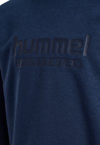 Marinblå sweatshirt i mjukt tyg med upphöjd svart logotyp "hummel" och "SPORTSWEAR" på framsidan. Slät yta, avslappnad design.