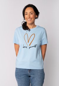 Hellblaues T-Shirt mit kurzen Ärmeln, das ein braunes Herz-Motiv und schwarzen Text "liebe dich selbst" auf der Vorderseite zeigt. Weicher Stoff.