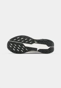 Semelle en caoutchouc noir avec des motifs de crantage texturés, incluant une partie intermédiaire blanche. Présente un talon incurvé et des zones latérales renforcées.