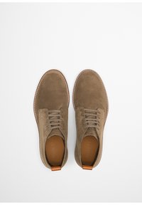 Chaussures en suede marron avec semelles en caoutchouc, bouts ronds et cinq paires d'œillets. Présentent une finition texturée et une languette de talon en cuir marron.
