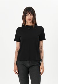 Čierne bavlnené tričko s krátkymi rukávmi, okrúhlym výstrihom a vyšitým logom "Calvin Klein" na hrudi. Jednoduchý dizajn, klasický strih.