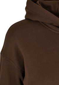 Sudadera con capucha marrón de textura suave, corte holgado y mangas ajustadas. Presenta un cuello alto y mínimos detalles de costura.