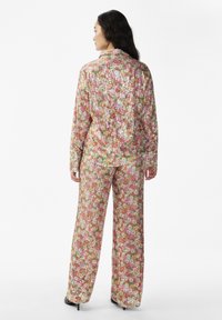 Costum format din două piese, cu imprimeu floral și strasuri, în culori pastelate, având o bluză cu o croială lejeră și pantaloni largi cu o suprafață texturată.