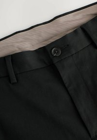 Schwarze Hosen mit glatter Textur, ausgestattet mit einem Knopfverschluss, Gürtelschlaufen und einem kontrastierenden beige gefütterten Taillenbund.