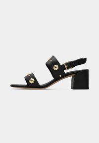 Black leather heeled sandals featuring two wide straps adorned with gold flower accents, a buckled ankle strap, and a square heel.
