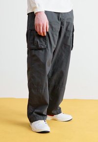 Pantalons cargo gris foncé en tissu léger, dotés de poches latérales et d'une coupe décontractée, associés à des baskets blanches.