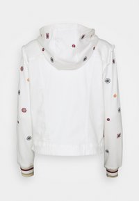 Chaqueta blanca con capucha, adornada con bordados florales circulares multicolores y puños de canalé a rayas, mostrada desde la parte posterior sobre un fondo blanco.