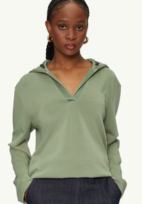 Groene hoodie met lange mouwen en een v-hals, voorzien van een verstelbare capuchon, gemaakt van zachte stof. Heeft een ontspannen pasvorm en zijzakken.
