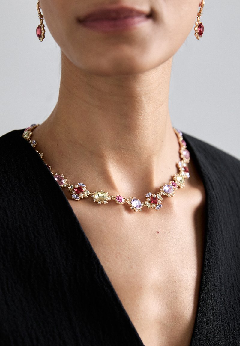 Kultainen kaulakoru ja siihen sopivat korvakorut, joissa on pinkkejä, purppuranvärisiä ja keltaisia jalokiviä, joissa on monimutkaiset asetelmat ja kukkakoristeet.